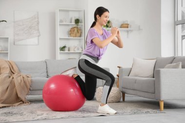 Sportif genç bayan evde spor topuyla egzersiz yapıyor.