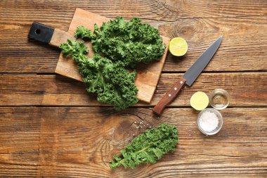 Tahta kesme tahtasında taze lahana yaprakları ve ahşap arka planda limon var.