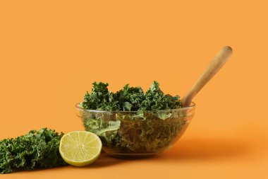 Turuncu arka planda taze lahana ve limon yapraklı cam kase.