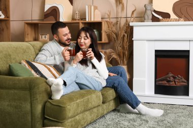 Evdeki şöminenin yanındaki kanepede oturmuş çay içen mutlu çifti seviyorlar.