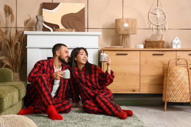 Evde şöminenin yanında sıcak çikolata bardakları olan damalı pijamalı mutlu çifti seviyorum.