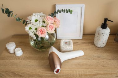Kozmetik ürünleri, mum ve çiçekli modern fotoepilatör banyoda lavabonun yanındaki masada.