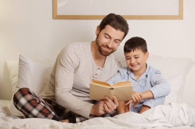 Babası ve küçük oğlu yatak odasında kitap okuyorlar.