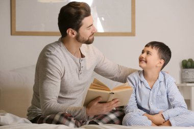 Babası ve küçük oğlu yatak odasında kitap okuyorlar.