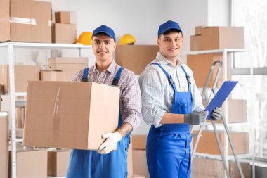 Depoda kutu ve pano taşıyan erkek yükleyiciler