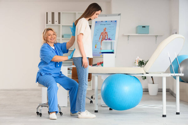 Зрелая счастливая женщина-остеопат работает с молодой женщиной в клинике