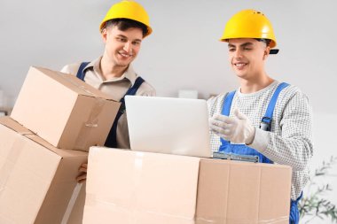 Erkek yükleyiciler ofiste dizüstü bilgisayar ve kutularla çalışıyorlar.