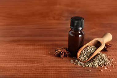 İçinde anason yıldızları, kurutulmuş tohumlar ve ahşap arka planda kepçe bulunan bir şişe gerekli yağ.