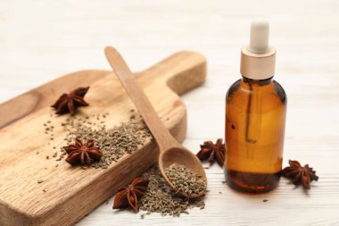 İçinde gerekli yağ şişesi, anason yıldızları, kurutulmuş tohumlar ve beyaz ahşap arka planda kaşık olan tahta.