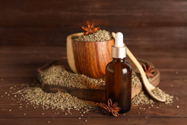 Bir şişe yağlı kaşık, anason yıldızları ve ahşap zemin üzerinde kurumuş tohumlar.