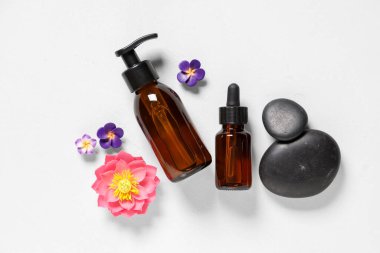 Hafif arka planda kozmetik ürünleri, spa taşları ve çiçeklerin bulunduğu kompozisyon