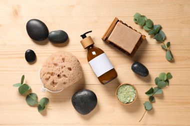 Kozmetik ürünleri, banyo süngeri, spa taşları ve okaliptüs dallarıyla ahşap zemin üzerinde kompozisyon