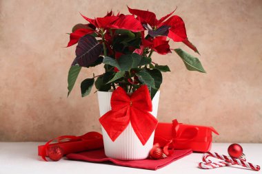 Noel çiçekleri süslemeli ve beyaz masada hediye kutusu var.