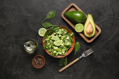 Bir kase lezzetli avokado salatası, ıspanak yaprakları ve siyah arka planda limon.