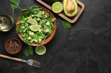 Bir kase lezzetli avokado salatası, ıspanak yaprakları ve siyah arka planda limon.