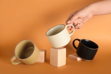 Farklı seramik bardaklara ve turuncu arka planda alçı podyumlara sahip kadın eli.