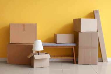 Hareket gününde oturma odasındaki sarı duvarın yanında gri banklı ve lambalı karton kutular.