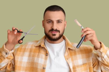 Elinde makas ve yeşil arka planda açık jilet olan yakışıklı, sakallı bir adam.