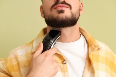 Yeşil arka planda elektrikli traş makinesi olan yakışıklı, sakallı bir adam.