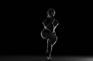 Siyah arka planda yoga yapan genç bir kadının silueti.