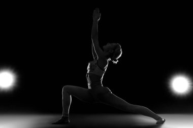 Siyah arka planda yoga yapan genç bir kadının silueti.