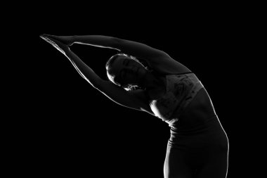 Siyah arka planda yoga yapan genç bir kadının silueti.