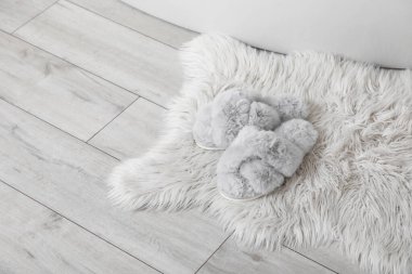 Banyoda küvetin yanında halının üzerinde yumuşak terlikler, yakın plan.