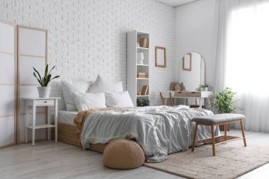 Yatak odasının içinde tuvalet masası, raf ünitesi ve beyaz tuğla duvarın yanında yatak.