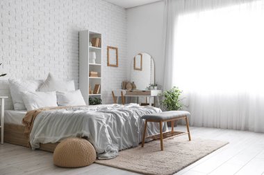 Yatak odasının içinde tuvalet masası, raf ünitesi ve beyaz tuğla duvarın yanında yatak.