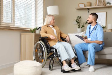 Erkek doktor evde tekerlekli sandalyede olgun bir kadınla çalışıyor.