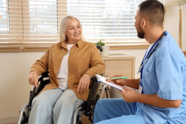 Erkek doktor evde tekerlekli sandalyede olgun bir kadınla çalışıyor.