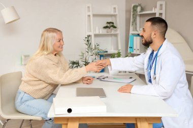 Klinikteki masada tokalaşan olgun bir kadınla erkek doktor.