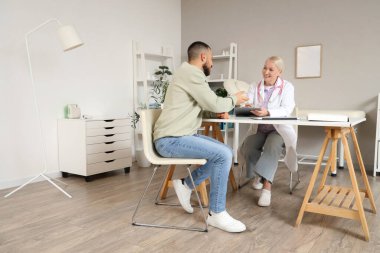 Klinikteki masada genç bir adamla çalışan kadın doktor.