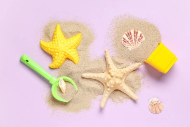 Kum, deniz kabuğu, oyuncak kürek ve pembe arka planda plaj oyuncağı kalıpları.