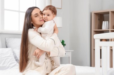 Pijamalı genç bir anne yatak odasında bebeğine sarılıyor. Uluslararası Sarılma Günü