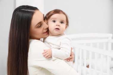 Pijamalı genç bir anne yatak odasında bebeğine sarılıyor. Uluslararası Sarılma Günü