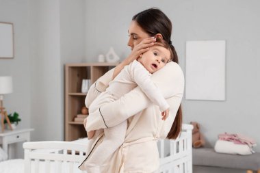 Pijamalı genç bir anne yatak odasında bebeğine sarılıyor. Uluslararası Sarılma Günü