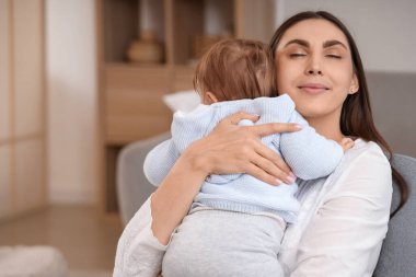 Genç bir anne bebeğini koltukta kucaklıyor. Uluslararası Sarılma Günü