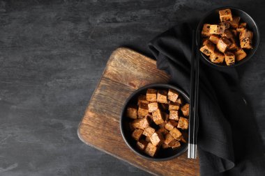 Siyah arka planda kızarmış tofu peyniri ve çubuklarla dolu kaseler.