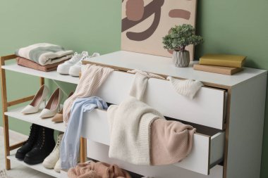 Ayakkabılı raf ünitesi ve dağınık giysiler yeşil duvarın yanındaki tuvalette, yakın plan.