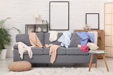 Gri kanepesi, kahve masası ve dağınık giysileri olan dağınık bir oturma odası.