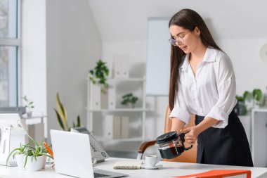 Ofisteki masada kahveye kahve dolduran genç sekreter.