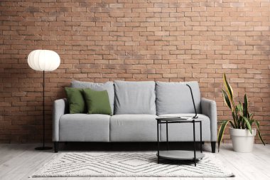 Oturma odasının içinde gri kanepe, masa ve parlayan lamba var.