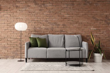 Oturma odasının içinde gri kanepe, masa ve parlayan lamba var.