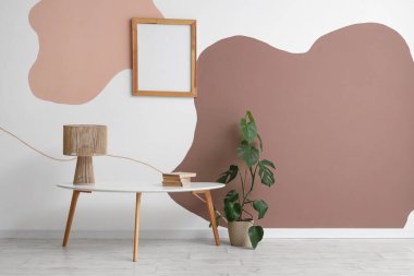 Renkli duvarın yanında ev bitkisi, lamba ve fotoğraf çerçeveli şık bir sehpa.