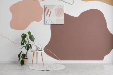 Renkli duvarın yanında bitki, halı ve boya bulunan şık bir sehpa.