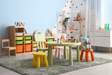 Çocuk oyun odasının içinde masa, raf üniteleri ve farklı oyuncaklar var.
