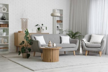 Beyaz tuğla duvarın yanında kanepesi, koltuğu ve şık sehpası olan modern oturma odasının içinde.