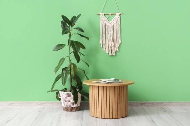 Yeşil duvarın yanında dekoru ve bitkisi olan şık bir kahve masası.