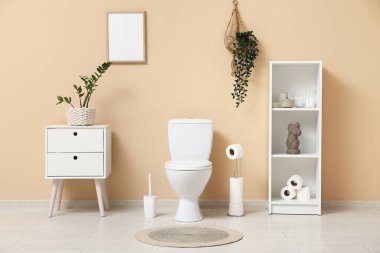 Tuvaletin içinde klozet, raf ünitesi ve bej duvarın yanındaki komodinin yanında.